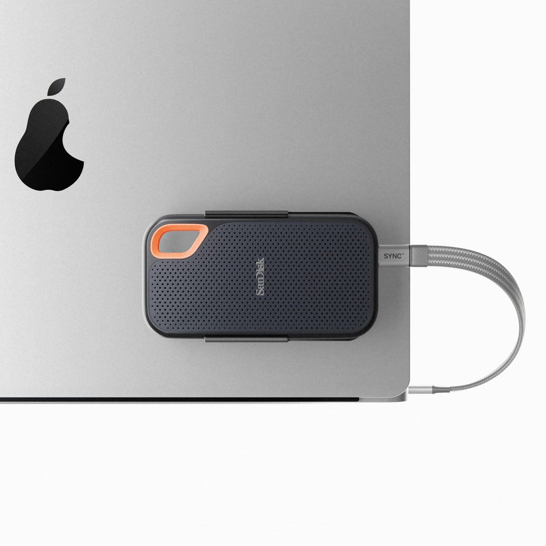 An external SSD dangling from a laptop USB-C cable on a cafe table