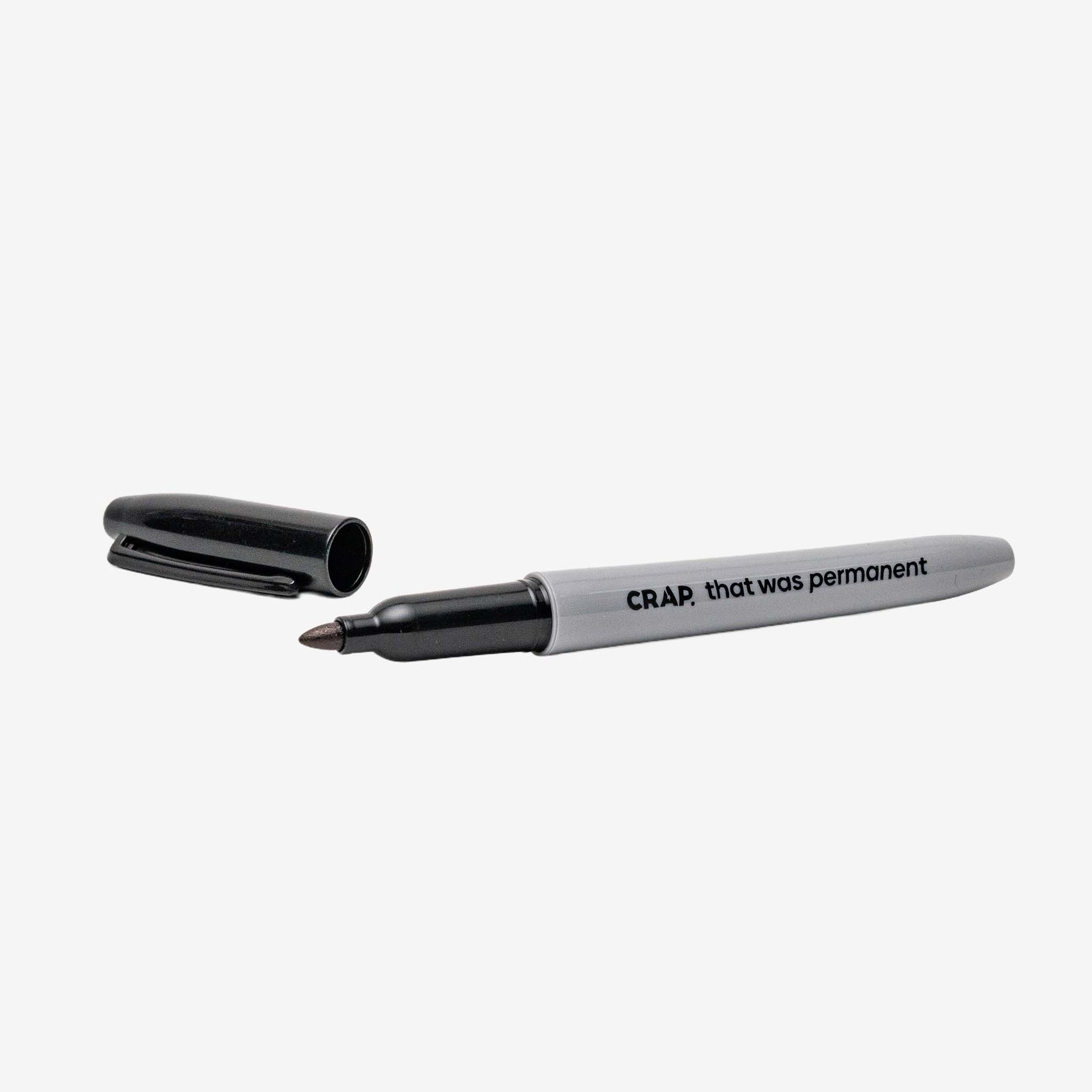 Fine-tip permanent marker with "CR.A.P. that was permanent" text on grey barrel and black cap removed, isolated on white background