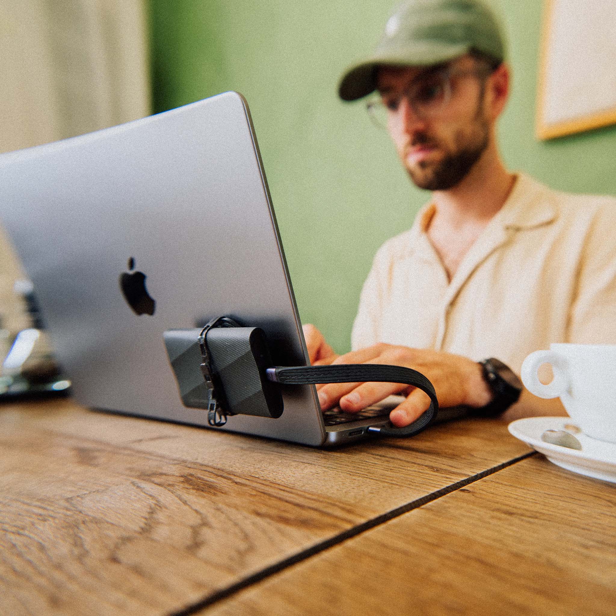 Man in casual clothing working on a laptop with an external SSD connected on a wooden table with a coffee cup nearby