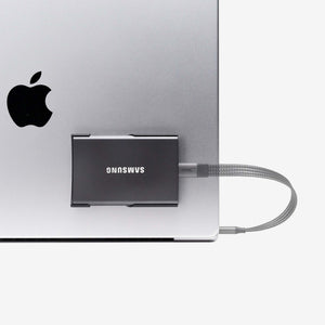 Compact black SCREENMOUNT securely attached to a laptop, holding a Samsung T-series drive to prevent dangling.