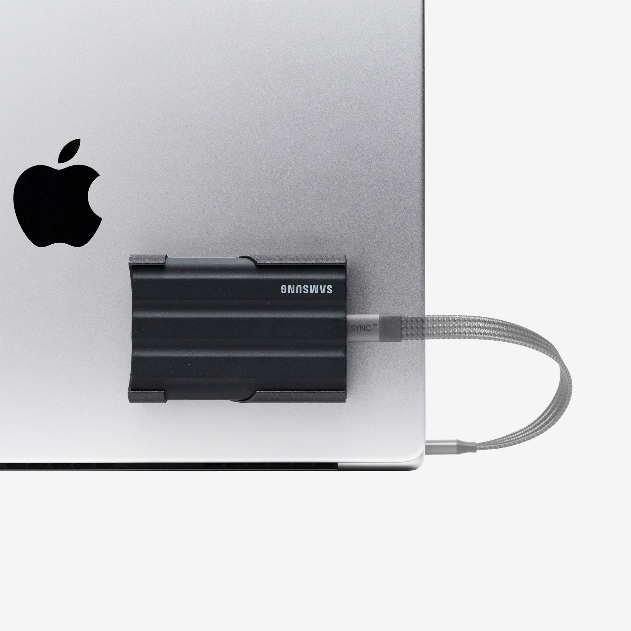 Black SCREENMOUNT securely holding a Samsung T-series drive attached to a silver laptop to prevent dangling.