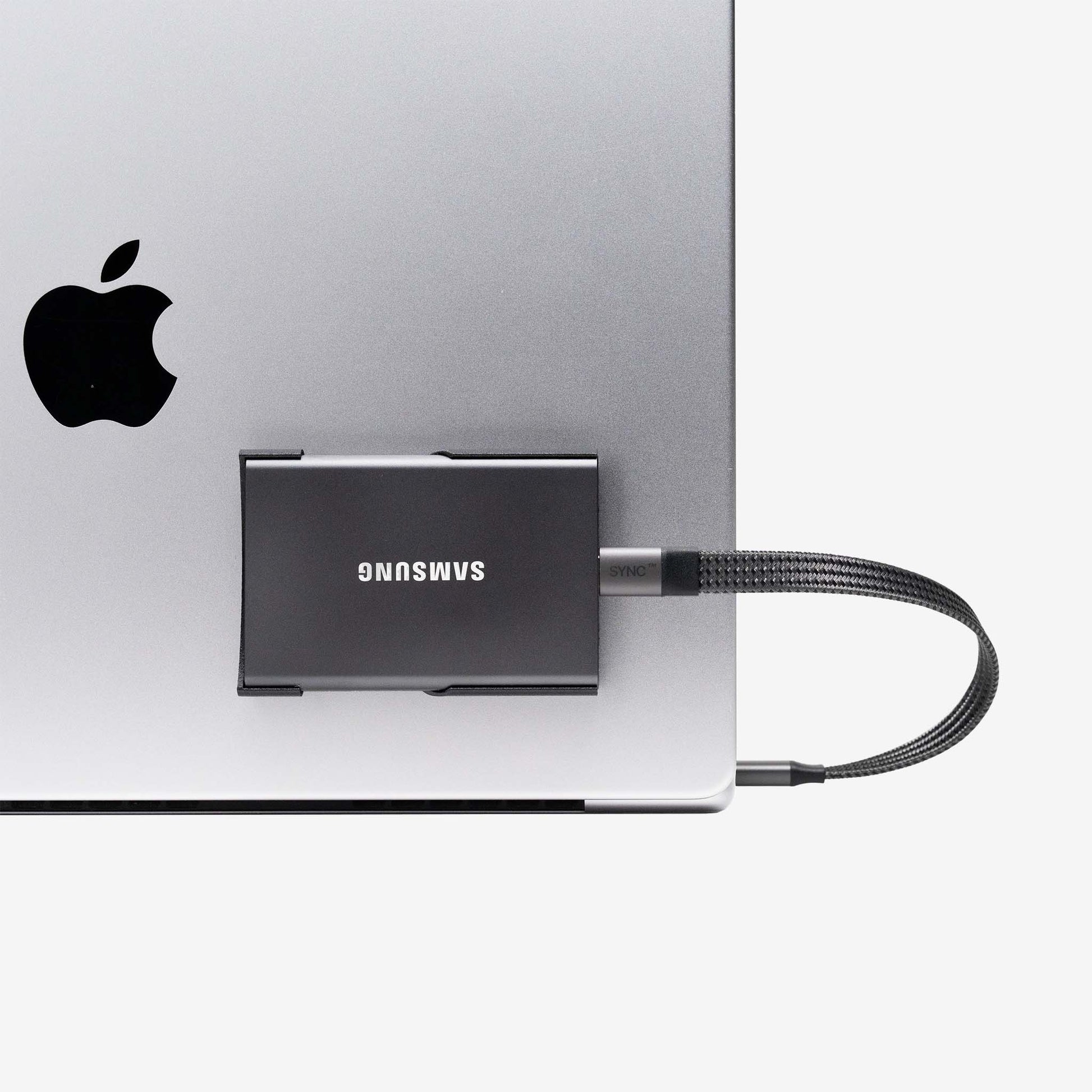 Black SCREENMOUNT holding a Samsung T-series drive securely attached to a silver laptop’s side port.
