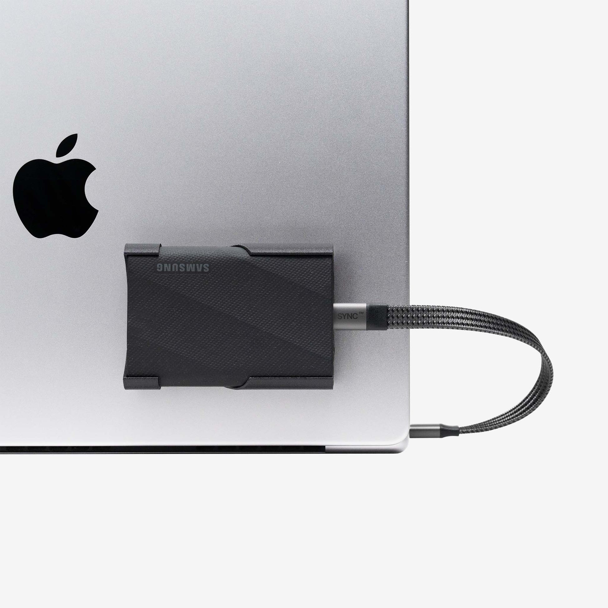 Close-up of Samsung SCREENMOUNT securing a Samsung T-series drive to a silver Apple laptop for organized connectivity.