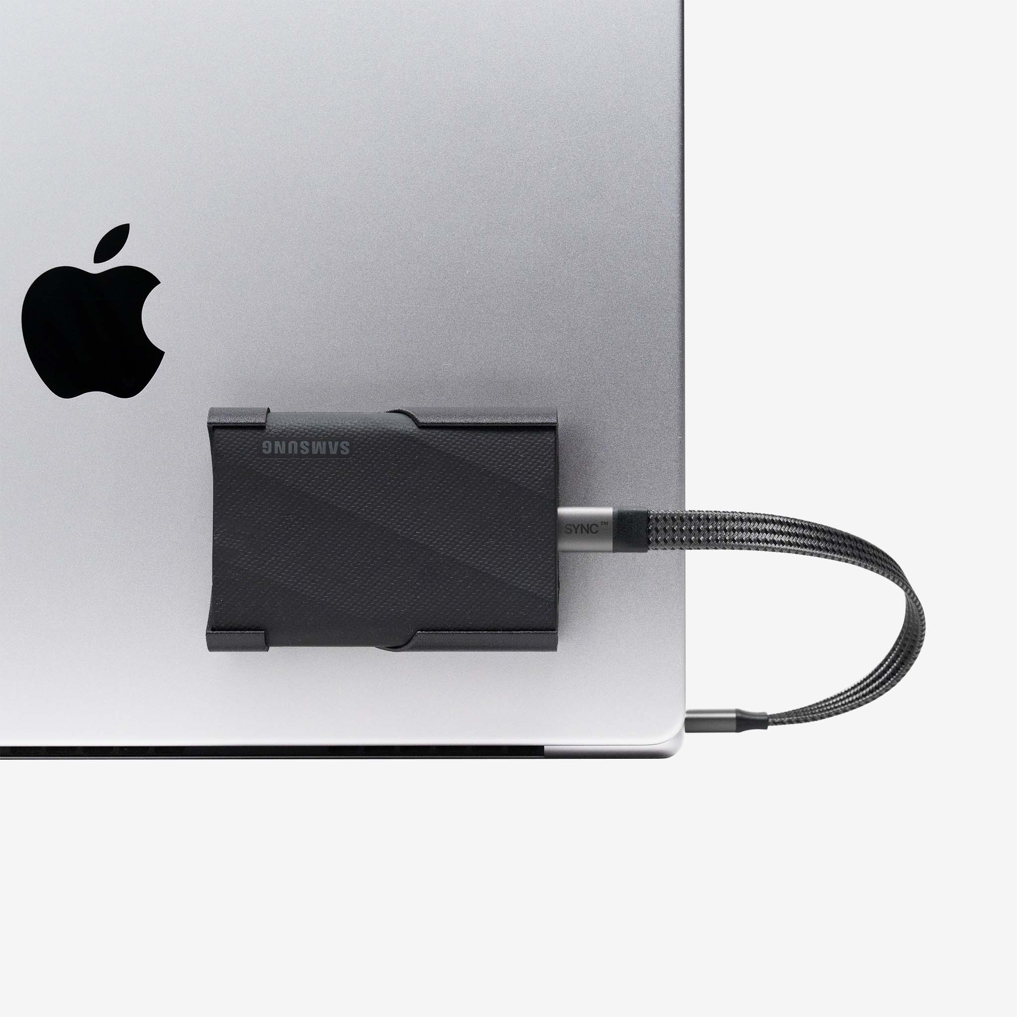 Close-up of Samsung SCREENMOUNT securing a Samsung T-series drive to a silver Apple laptop for organized connectivity.