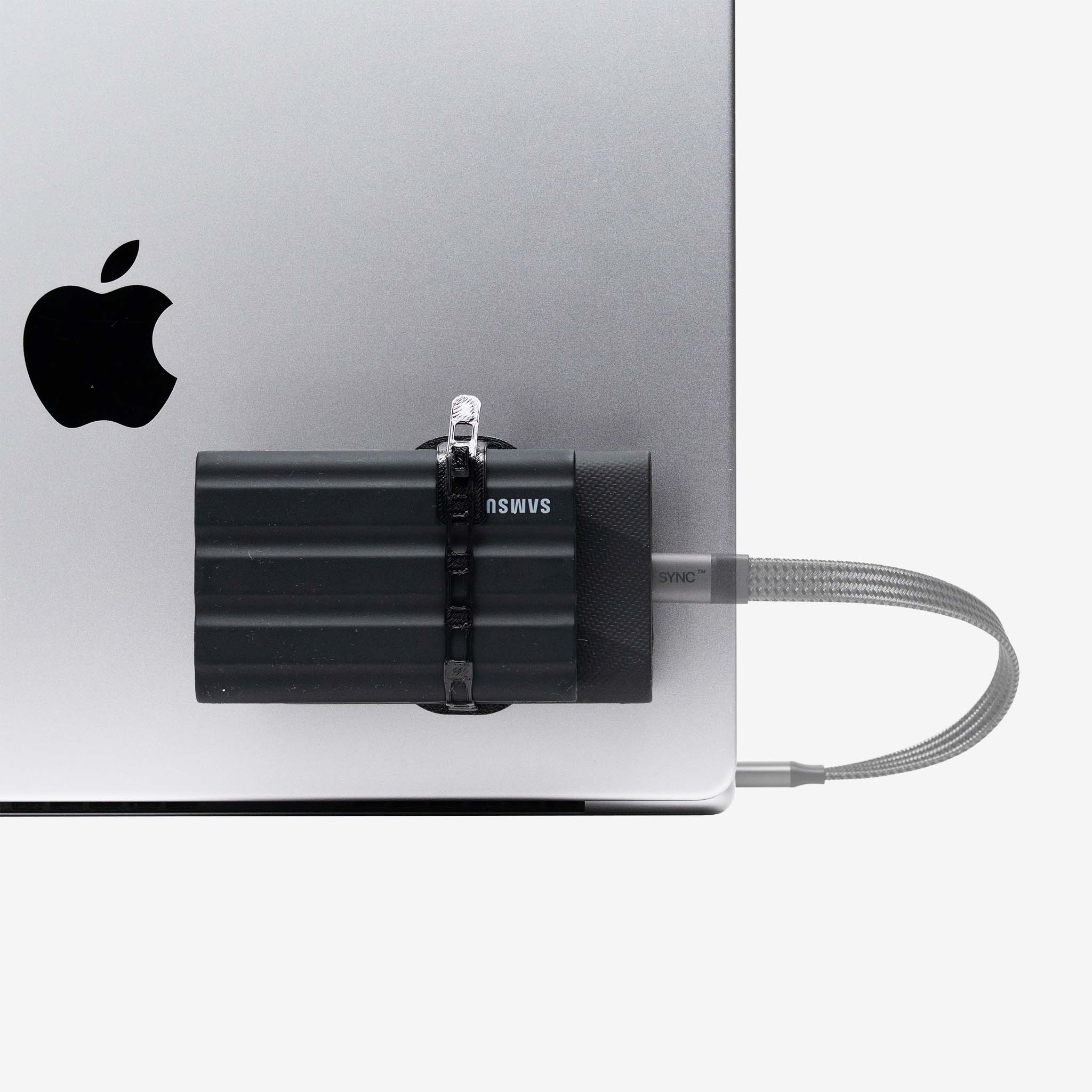 Universal SCREENMOUNT holding a Samsung external drive attached to the side of a silver laptop with a connected cable