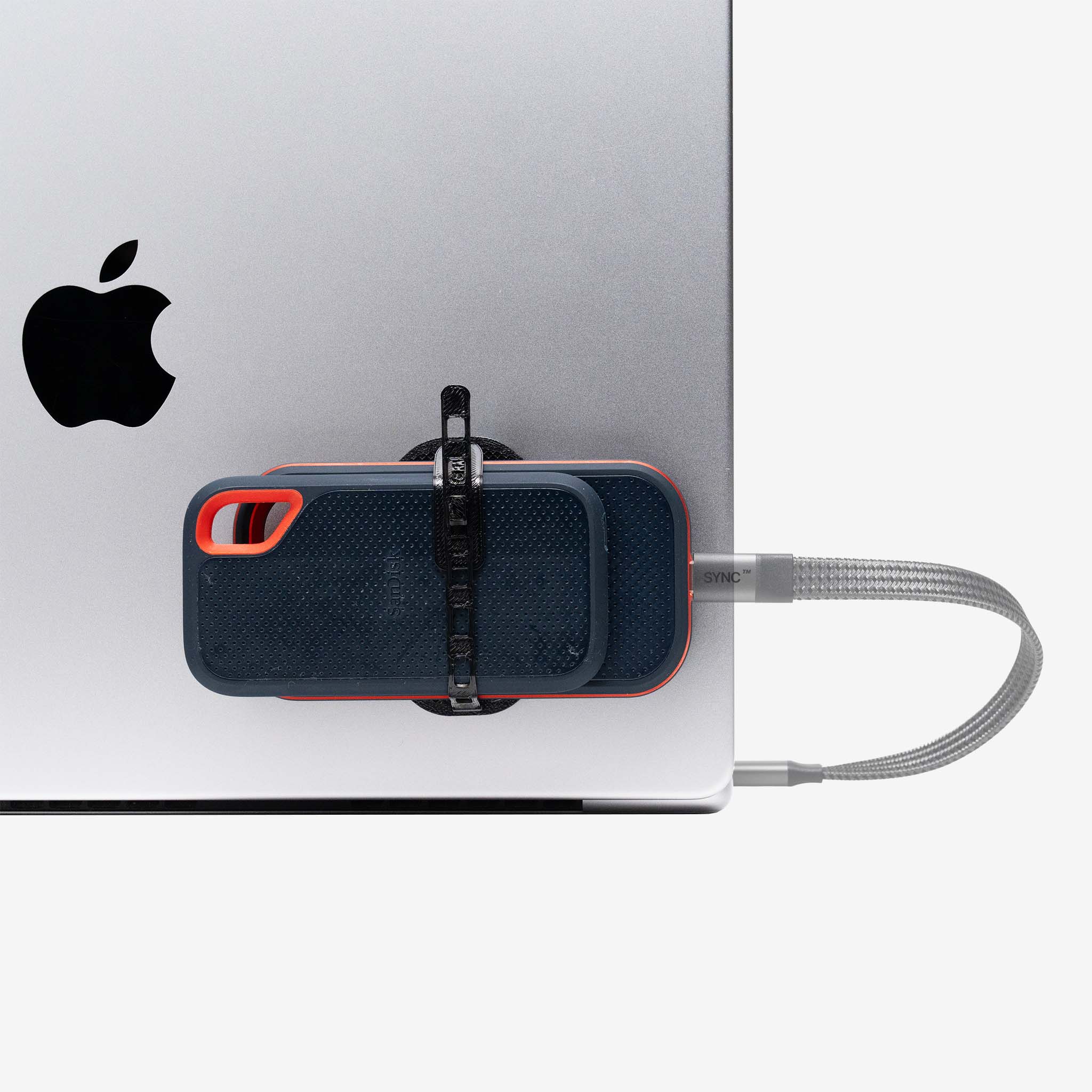 Universal SCREENMOUNT holding a portable drive attached to the side of a silver Apple laptop with a connected cable.