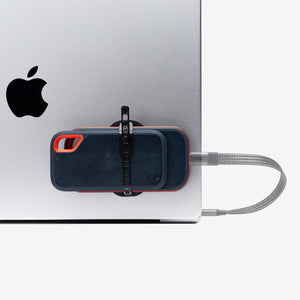 Universal SCREENMOUNT holding a portable drive attached to the side of a silver Apple laptop with a connected cable.