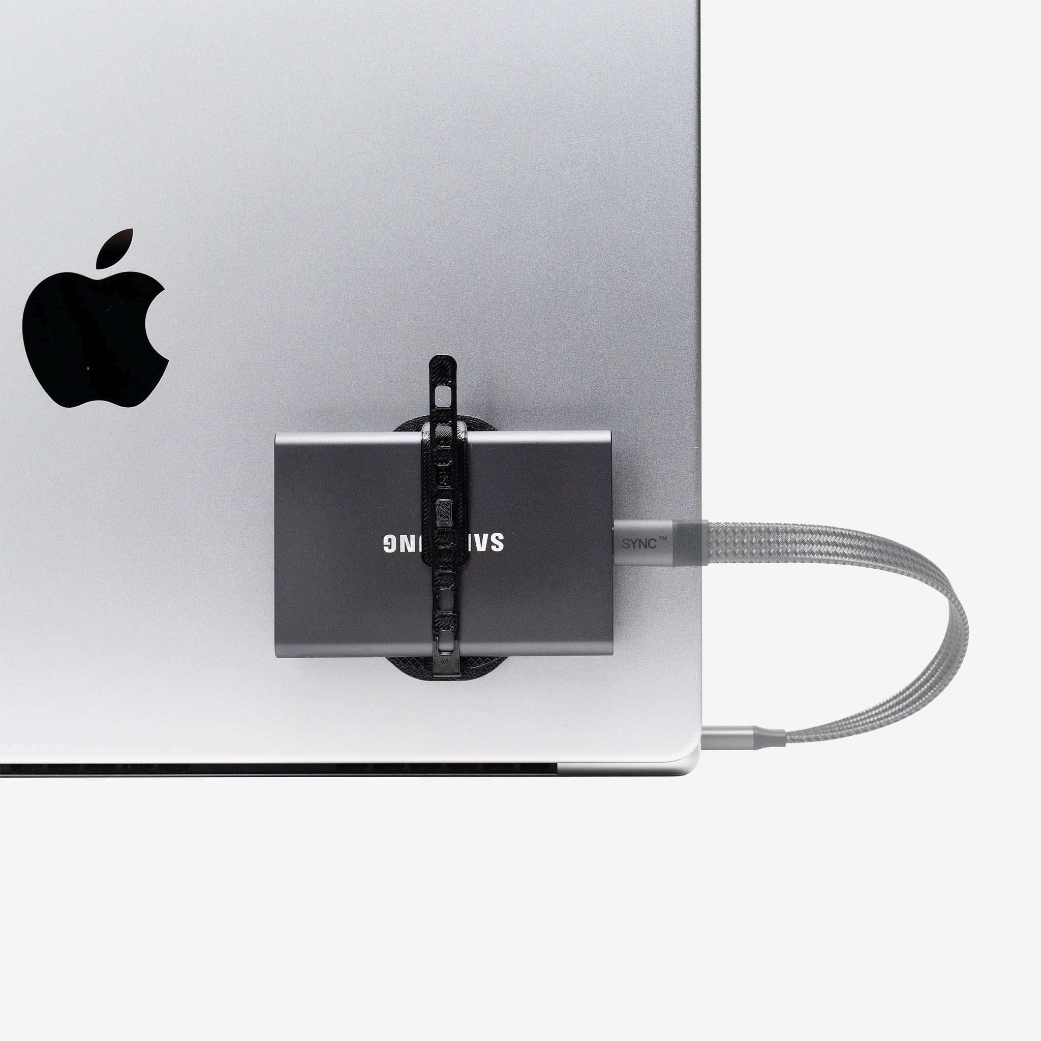 Samsung external drive mounted on the back of a silver MacBook using a universal SCREENMOUNT holder with a connected cable